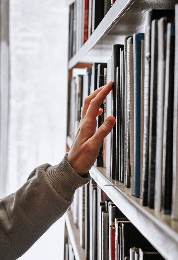 A person's hands going through books on a bookshelf