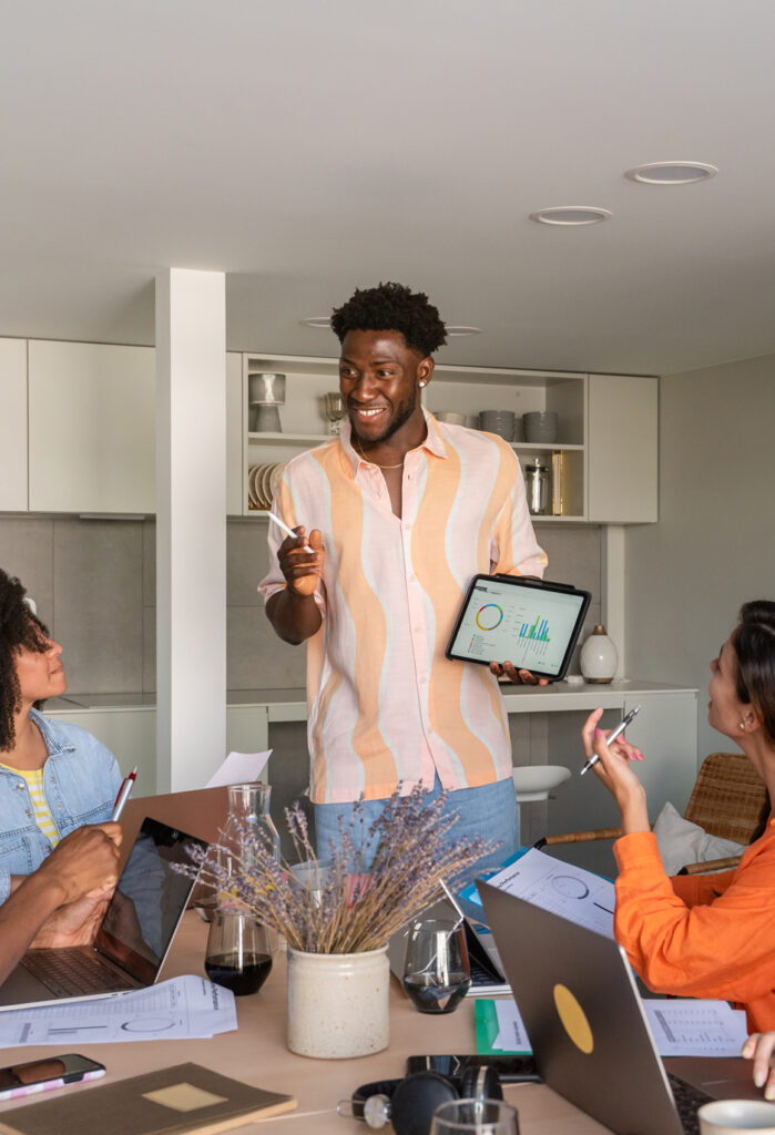 Standing man presenting charts on a tablet to two other seated people