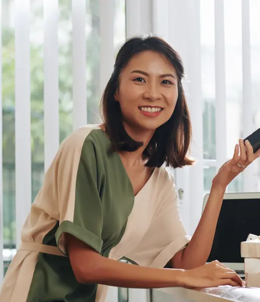 A woman with short black hair standing by a desk with a laptop and smiling