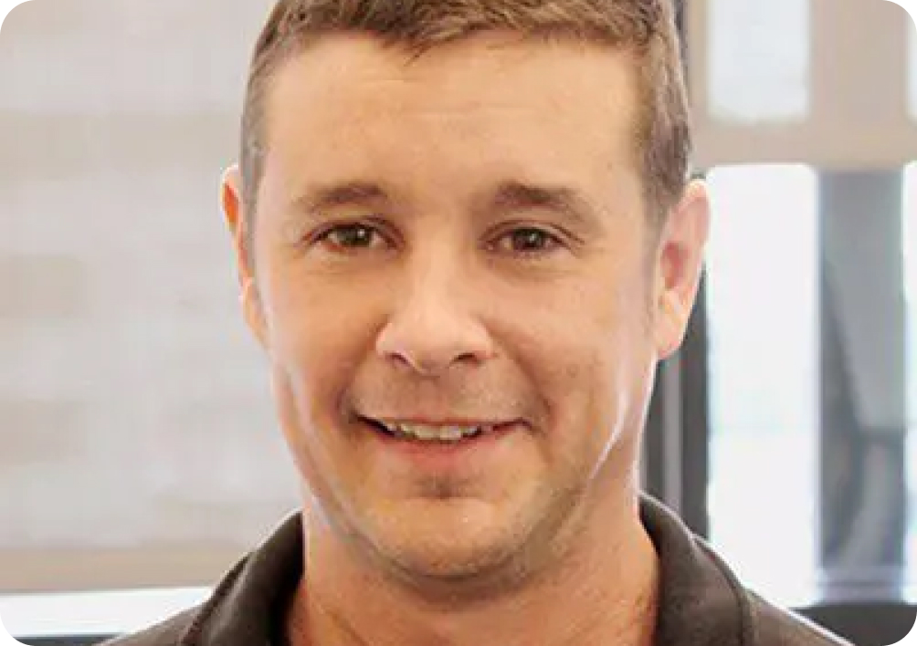 Light brown haired man smiling in a dark brown collared shirt.