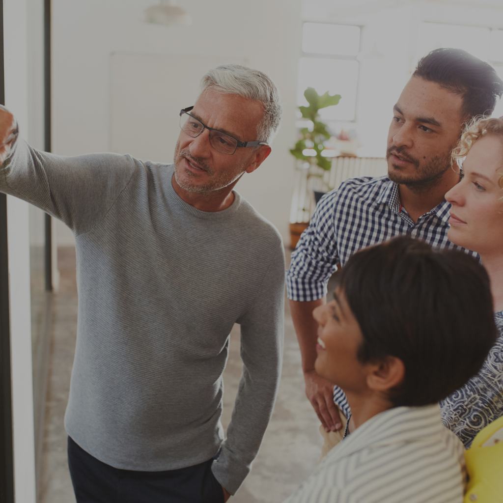 Man explaining, three people attentively watching.