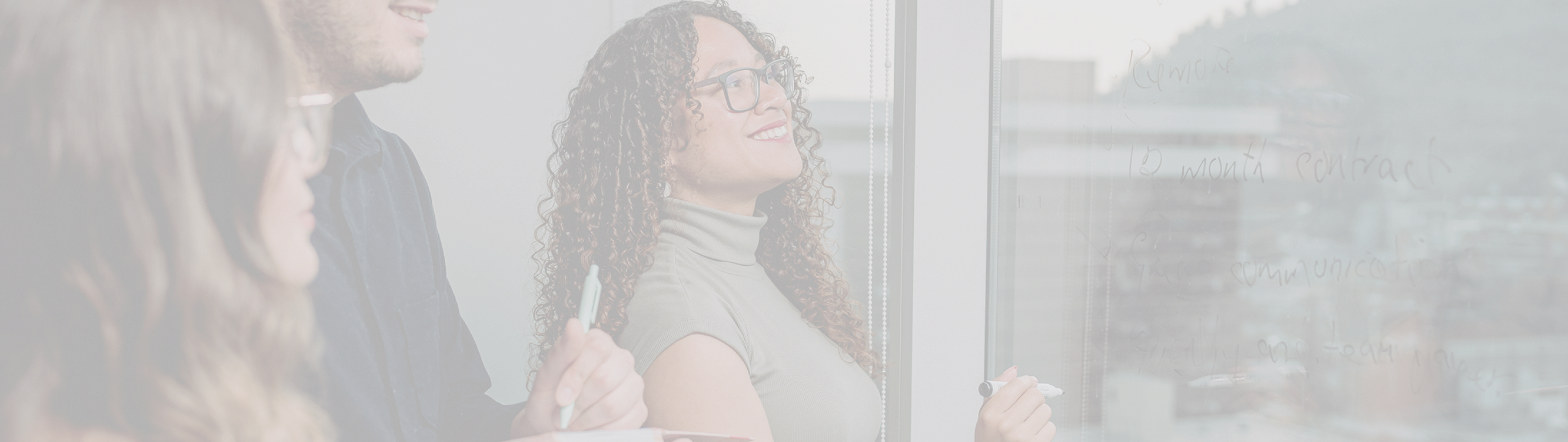 Happy woman holding a pen, examining a glass with written notes, accompanied by a man and another woman.