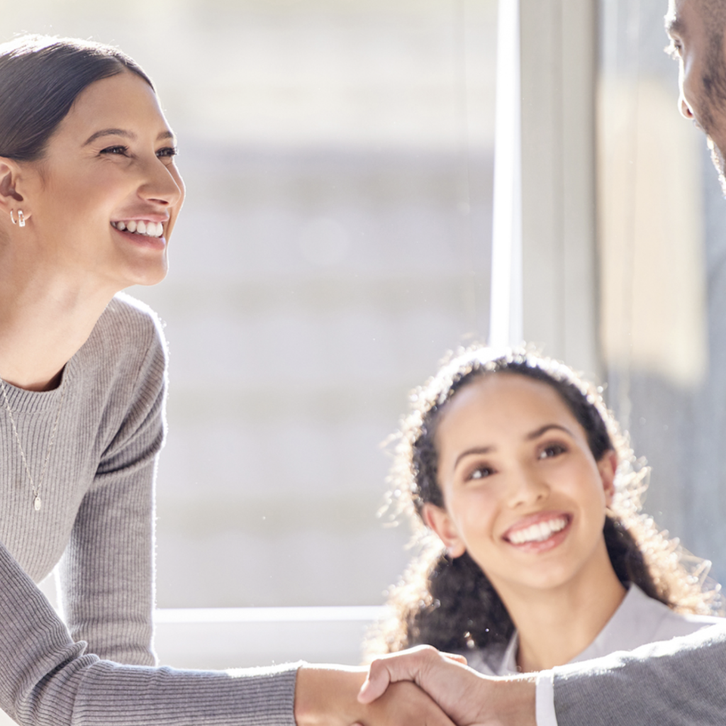 Two fair-haired women smiling, one of them shaking hands with a man.