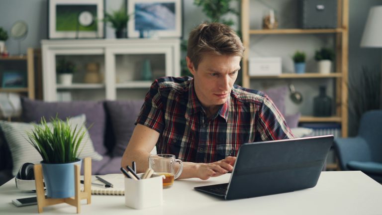 A blonde man in a plaid shirt using a laptop at a desk, possibly participating in an AI interview